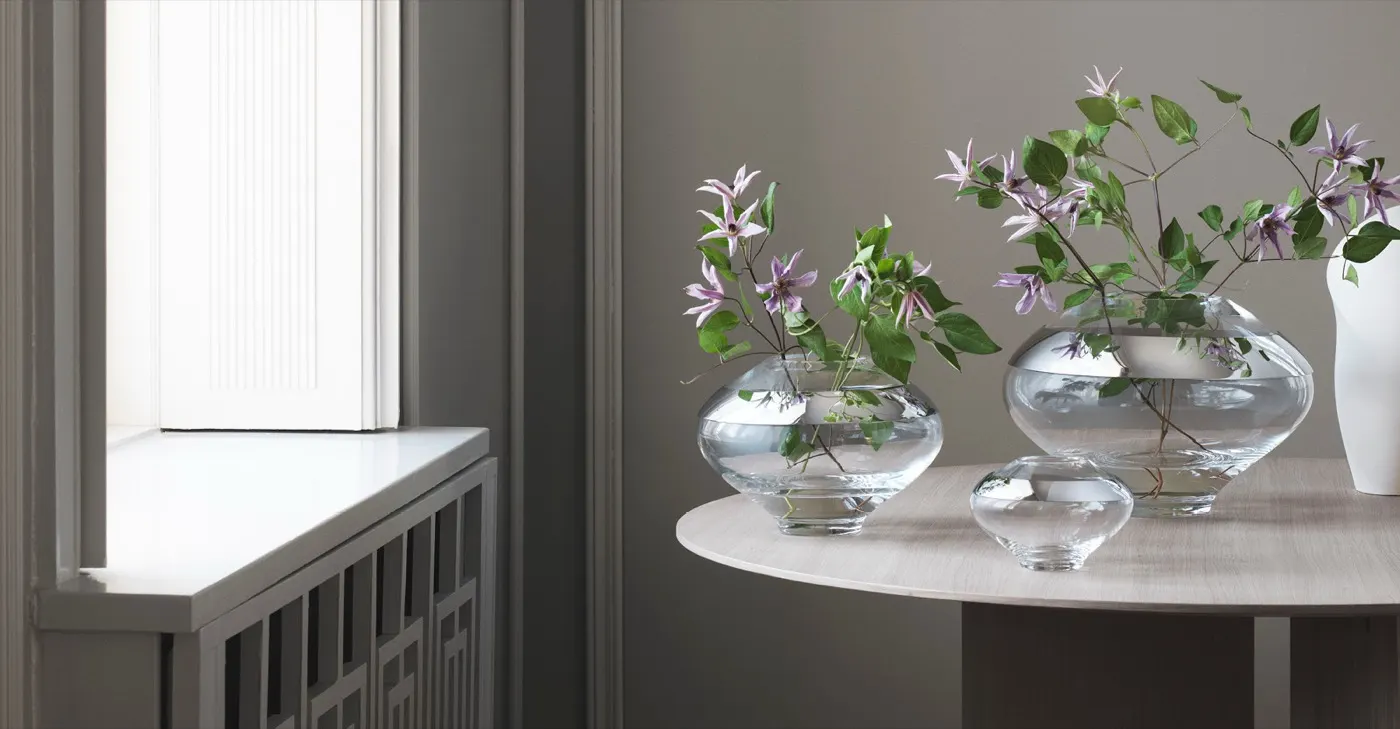 Mouth-blown glass vases with clematis flowers beside a bright window