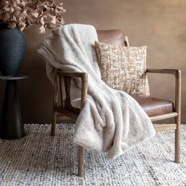 A beige fringed wool throw draped over an armchair